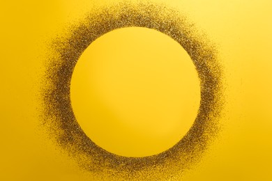 Photo of Frame made of shiny golden glitter on yellow background, top view. Space for text