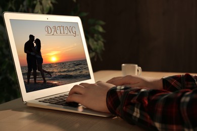 Man visiting dating site via laptop at wooden table indoors, closeup