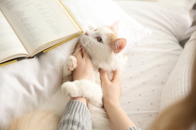 Woman with cute fluffy cat and book on bed, closeup