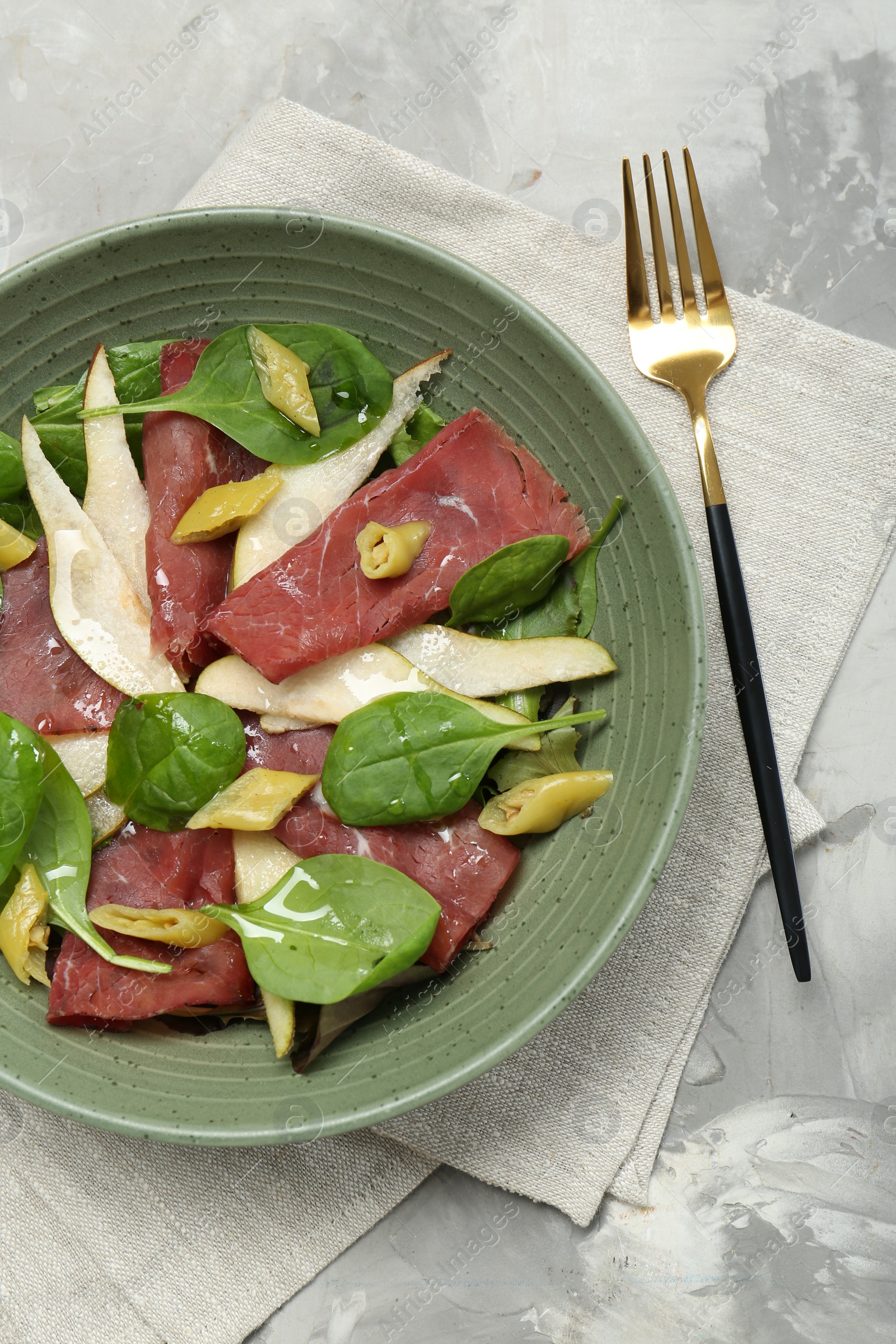 Photo of Delicious bresaola salad in bowl served on light grey textured table, flat lay