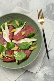 Delicious bresaola salad in bowl served on light grey textured table, flat lay