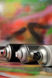 Photo of Cans of different graffiti spray paints on color background, closeup. Space for text`