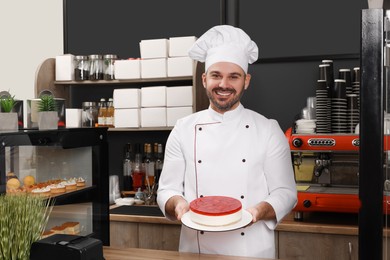 Photo of Happy baker showing delicious cheesecake in his cafe