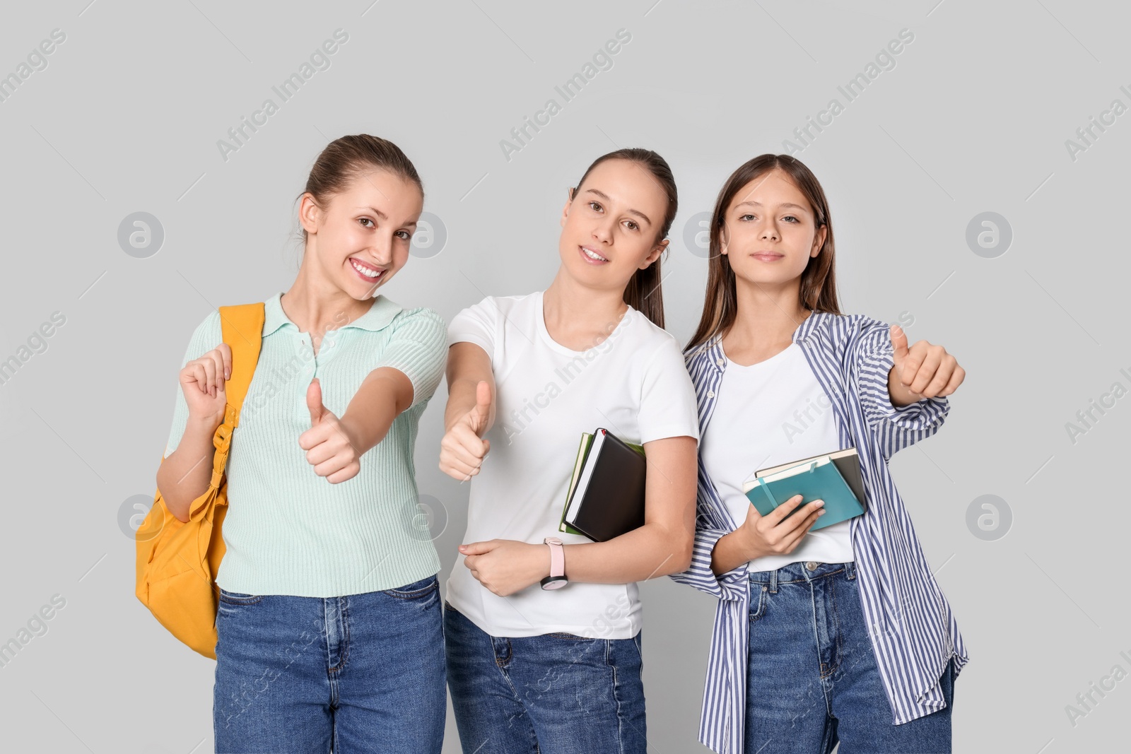 Photo of Teenage girls with books and backpack showing thumbs up on light grey background