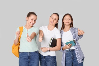 Photo of Teenage girls with books and backpack showing thumbs up on light grey background