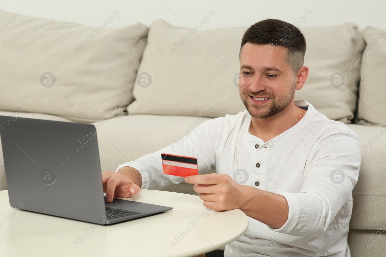 Photo of Happy man with credit card using laptop for online shopping at white table indoors