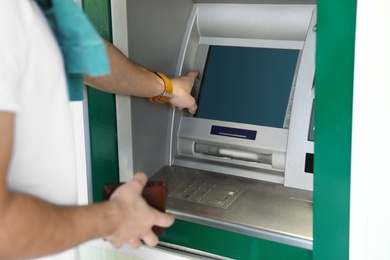 Photo of Young man using modern cash machine outdoors, closeup