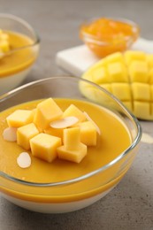 Photo of Delicious panna cotta with mango coulis and fresh fruit pieces on grey table, closeup