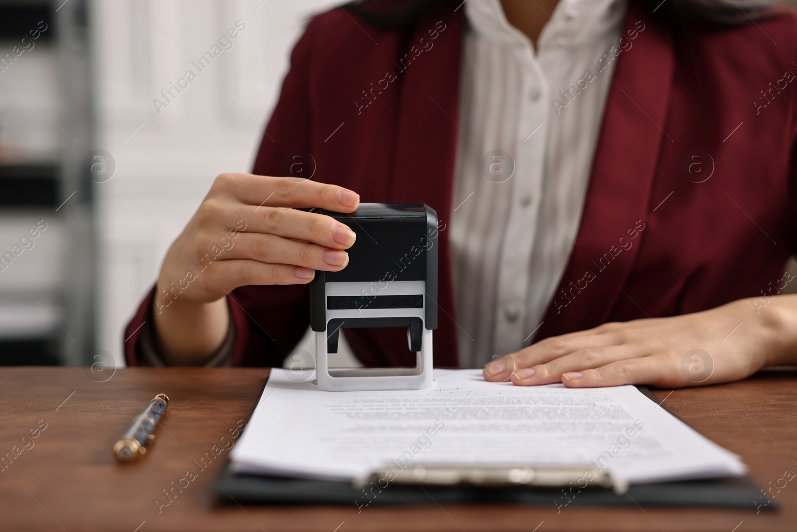 Photo of Notary stamping document at table in office, closeup