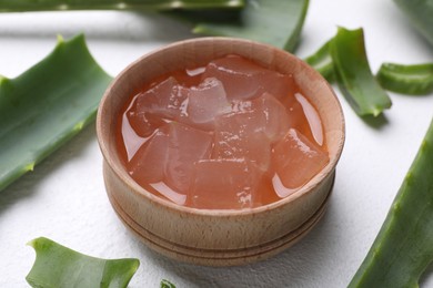 Photo of Aloe vera gel in bowl and slices of plant on white textured background, closeup