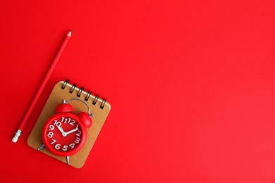 Alarm clock, notebook and pencil on red background, flat lay. Space for text