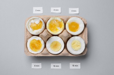 Different cooking time and readiness stages of boiled chicken eggs on light grey background, flat lay