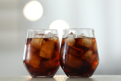 Photo of Glasses of cola with ice on table against blurred background