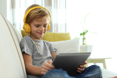 Photo of Cute little boy with headphones and tablet listening to audiobook at home