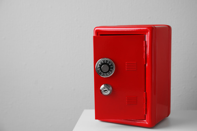 Photo of Red steel safe on table against light wall. Space for text