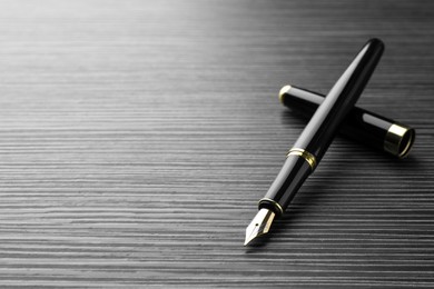Photo of Stylish fountain pen on black wooden table, closeup. Space for text