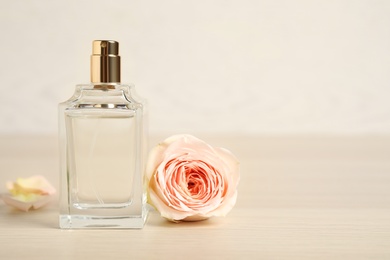 Photo of Bottle of perfume and beautiful rose on wooden table. Space for text