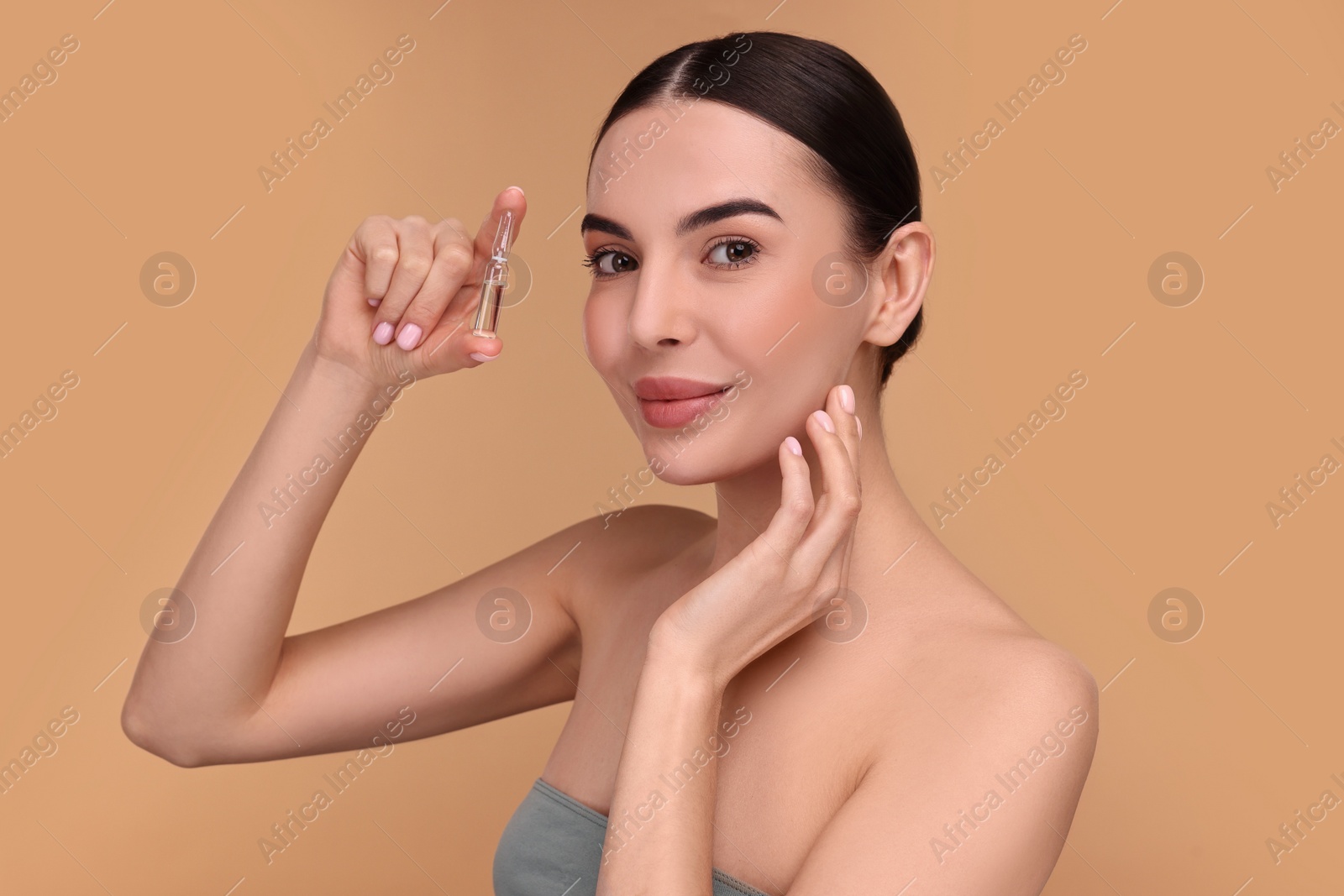 Photo of Beautiful young woman holding skincare ampoule on beige background