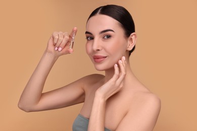 Beautiful young woman holding skincare ampoule on beige background