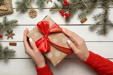 Woman with Christmas gift at white wooden table, top view