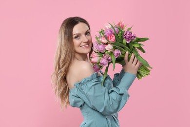 Happy young woman with bouquet of beautiful tulips on pink background