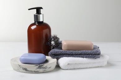 Photo of Soap bars, dispenser and terry towels on white marble table
