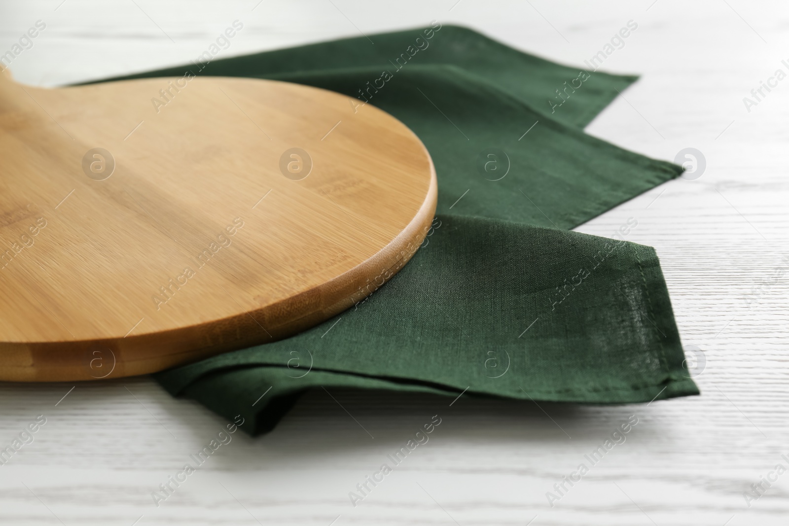 Photo of Empty wooden board and green napkin on white table, closeup