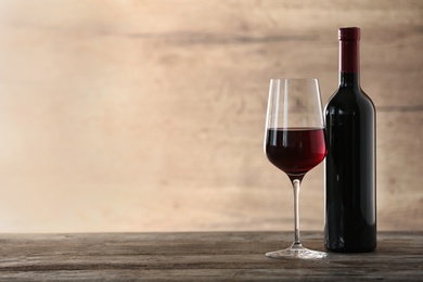 Glass and bottle of red wine on wooden table. Space for text