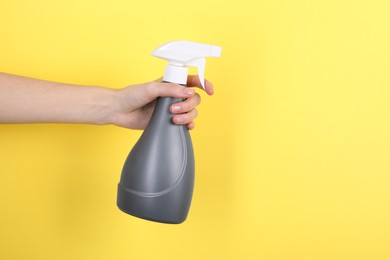 Woman holding plastic spray bottle on yellow background, closeup. Space for text