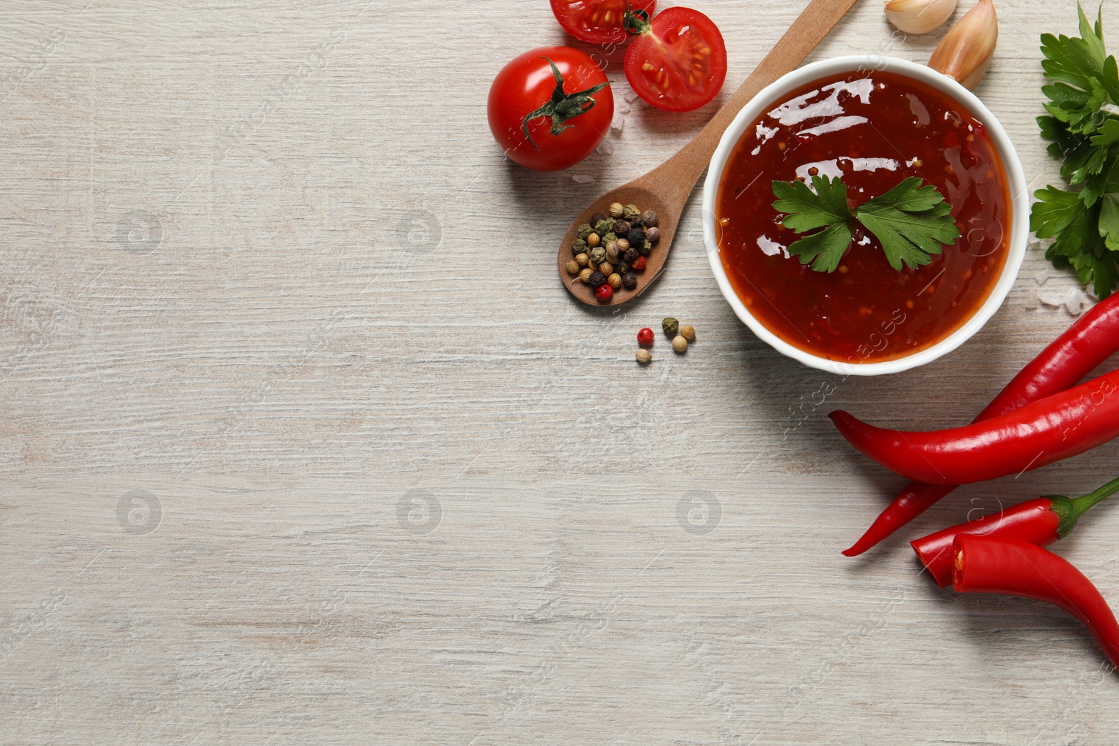 Photo of Spicy chili sauce and ingredients on white wooden table, flat lay. Space for text