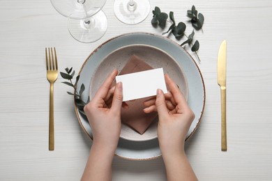 Photo of Woman holding adjusting stylish table setting with eucalyptus leaves and cutlery on white wooden background, closeup