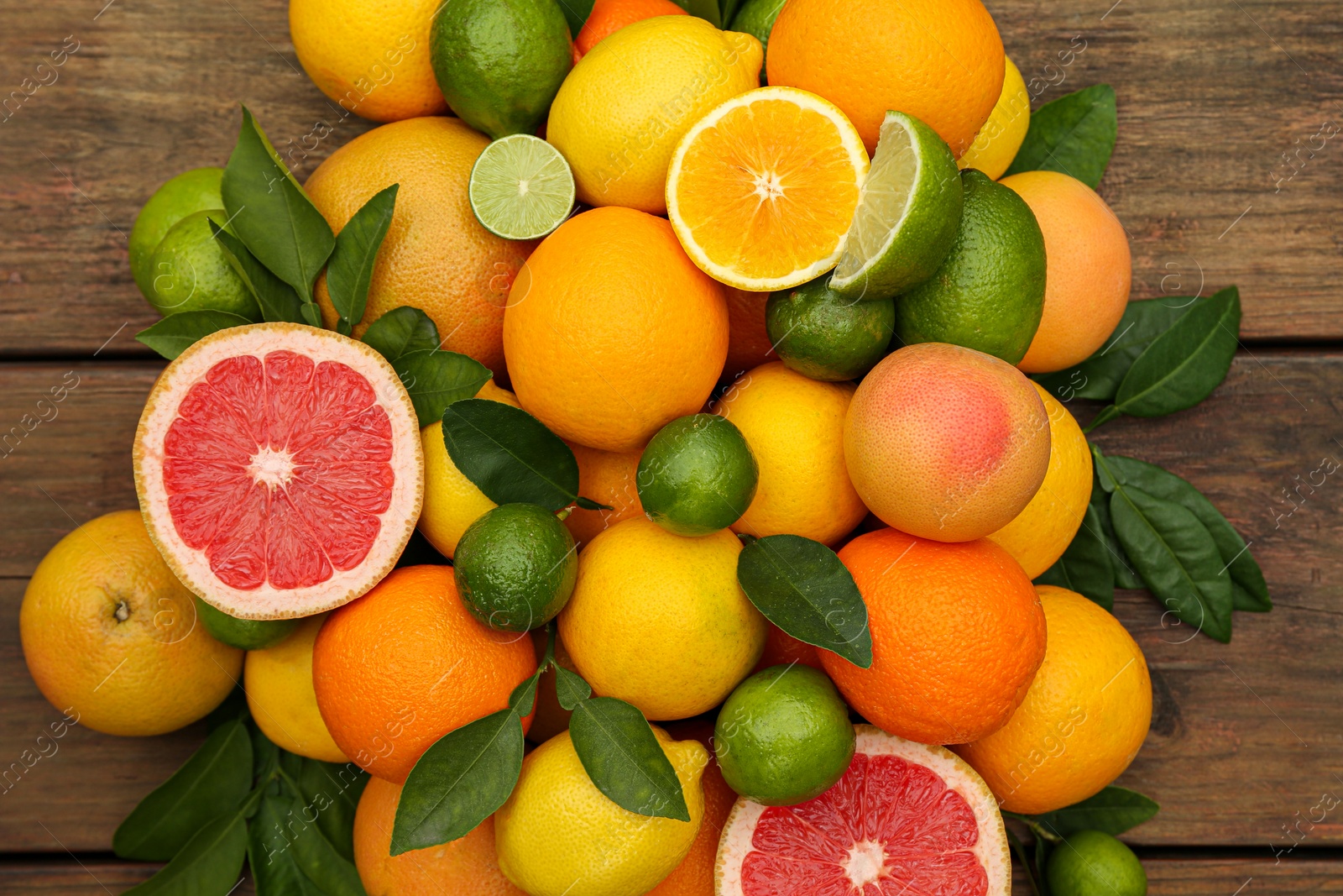 Photo of Different citrus fruits with green leaves on wooden table, flat lay