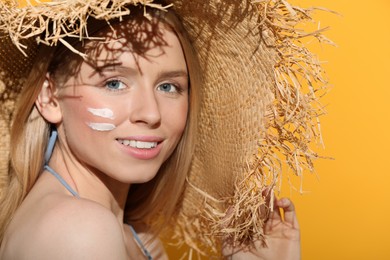 Beautiful young woman in straw hat with sun protection cream on her face against orange background