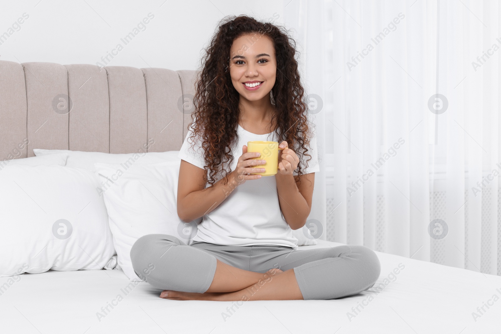 Photo of Happy African American woman with cup of drink in bed at home