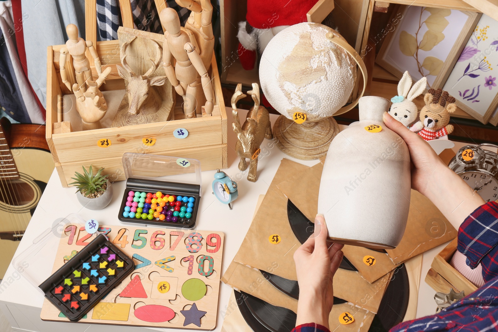 Photo of Woman holding vase near table with many different stuff, closeup. Garage sale