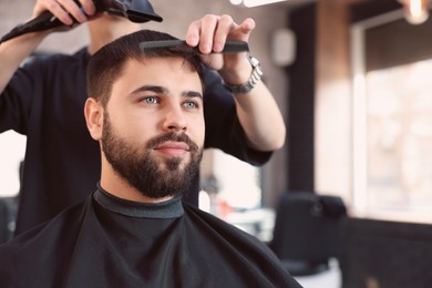 Professional hairdresser working with client in barbershop