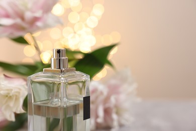 Bottle of perfume and beautiful lily flowers against beige background with blurred lights, closeup