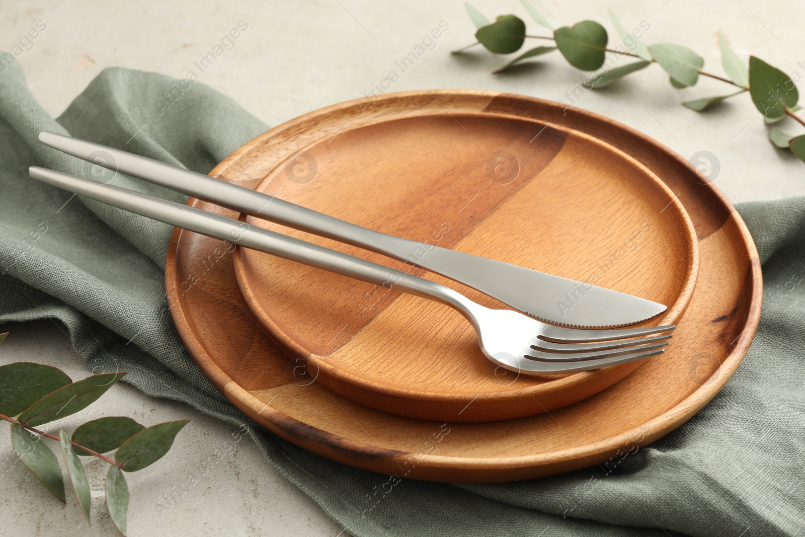 Photo of Stylish setting with cutlery, napkin, eucalyptus branches and plates on light table, closeup