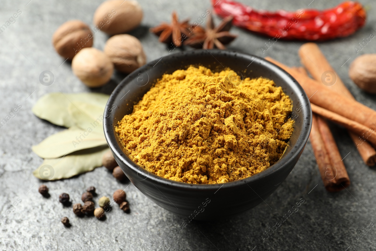 Photo of Dry curry powder in bowl and other spices on dark textured table, closeup