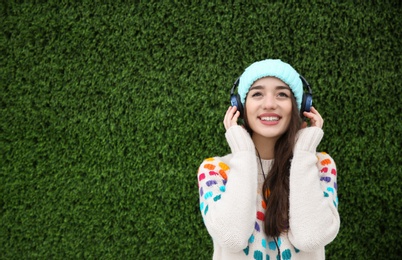 Photo of Beautiful young woman listening to music with headphones near grass wall. Space for text