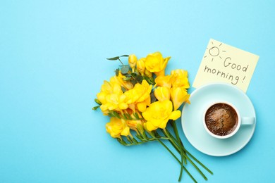 Photo of Cup of aromatic coffee, beautiful yellow freesias and Good Morning note on light blue background, flat lay. Space for text