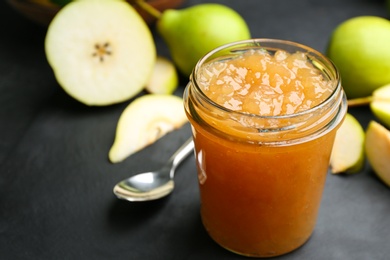Photo of Tasty homemade pear jam and fresh fruits on black table