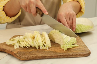 Photo of Woman cutting fresh chinese cabbage at table in kitchen, closeup