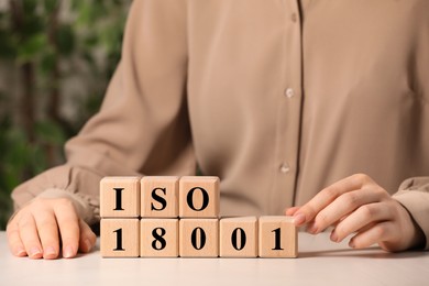 Photo of Woman making abbreviation ISO and number 18001 of wooden cubes at white table, closeup
