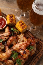 Delicious baked chicken wings, grilled corn and glasses of beer on wooden table
