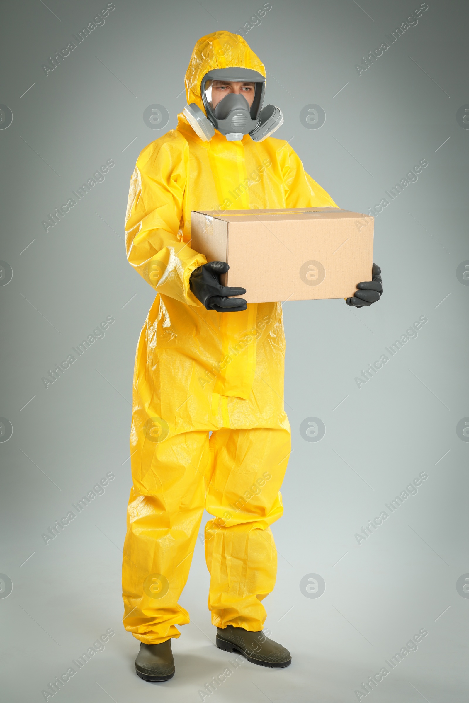 Photo of Man wearing chemical protective suit with cardboard box on light grey background. Prevention of virus spread