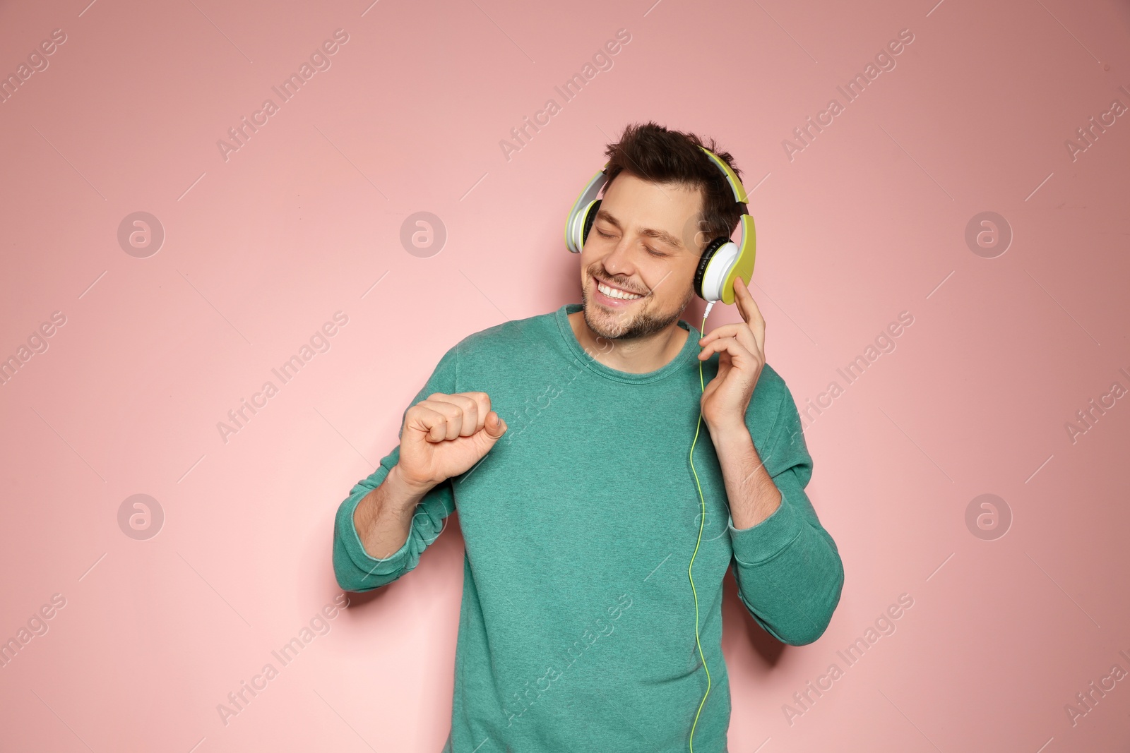 Photo of Handsome man listening to music with headphones on color background