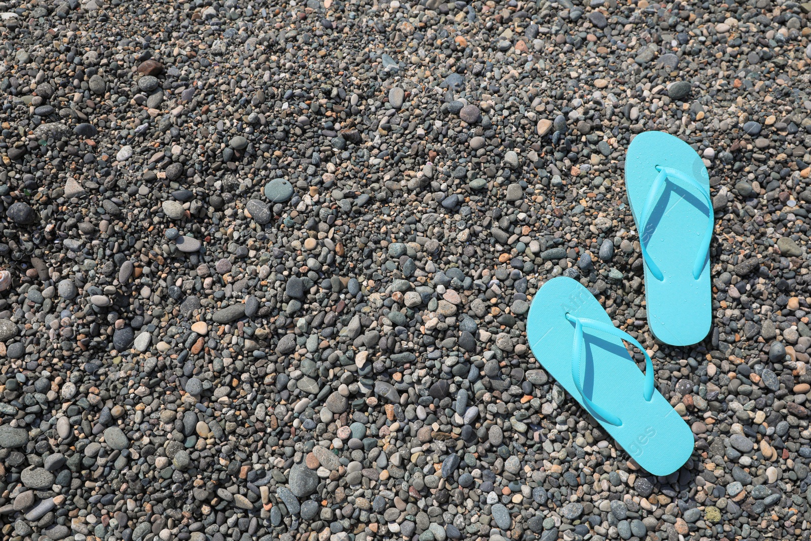 Photo of Stylish turquoise flip lops on pebble beach, above view. Space for text