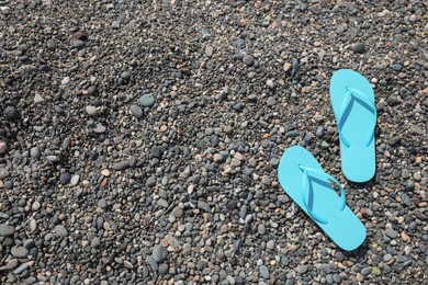 Stylish turquoise flip lops on pebble beach, above view. Space for text