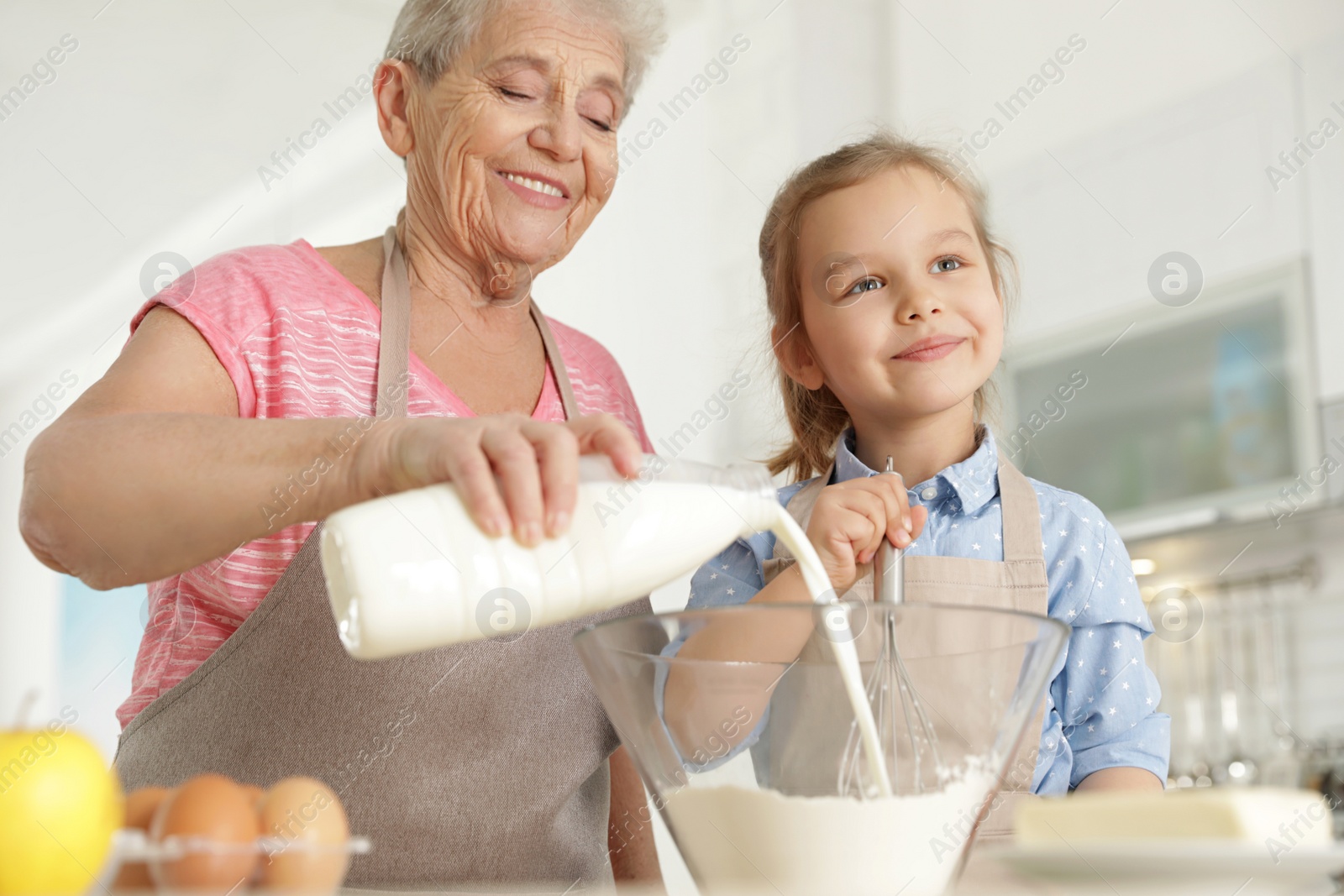 Photo of Cute girl and her grandmother cooking in kitchen